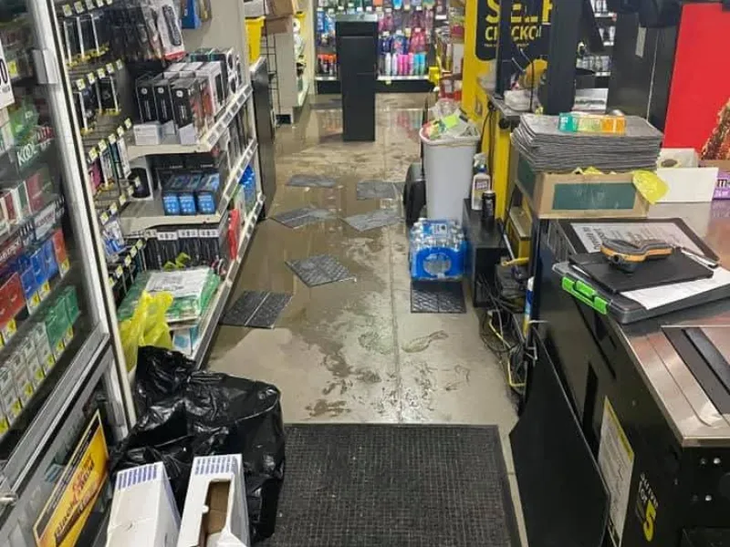 Store aisle with wet floor, scattered mats, and various products on shelves and counters.