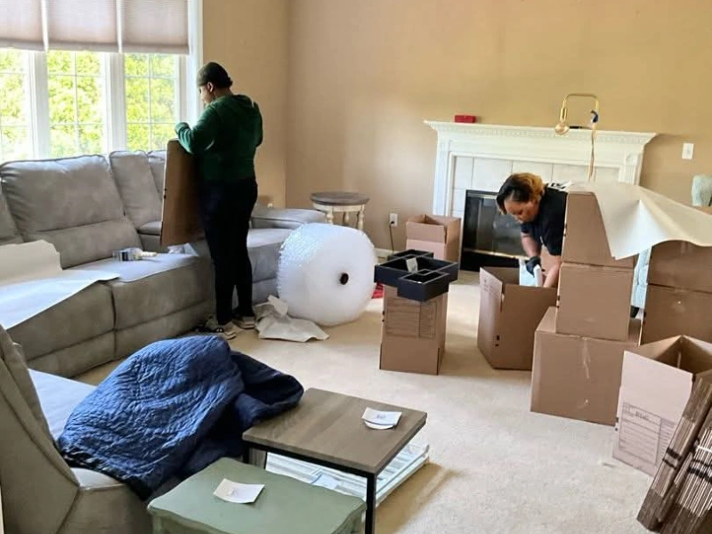 Two people packing boxes in a living room with a couch, bubble wrap, and furniture.